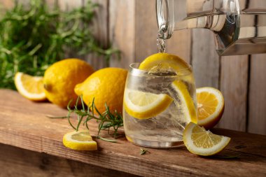 Eski ahşap bir masada buzlu, biberiyeli ve limonlu yaz ferahlatıcı bir içecek. Su bir sürahide buz ve limon dilimleri ile bir bardağa dökülür..