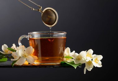 Bir fincan yasemin çayı ve siyah arka planda taze yasemin çiçekleri. Boşluğu kopyala.