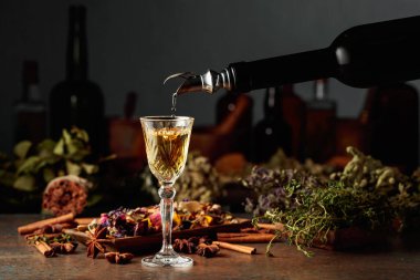 Sarı bitkisel likör ya da karışım eski bir şişeden bardağa dökülür. Kurutulmuş otlar, çiçekler, baharatlar ve eski mutfak aletleri. Bitkisel ilaç kavramı.