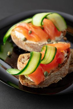 Siyah tabakta füme alabalık, krem peynir, taze salatalık ve kapari..