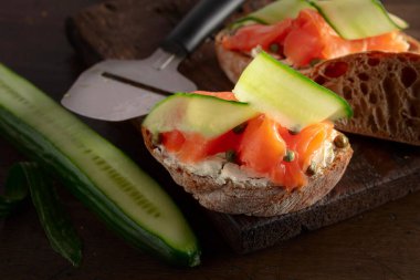 Tütsülenmiş alabalık, krem peynir, taze salatalık ve eski ahşap bir masada kapari..