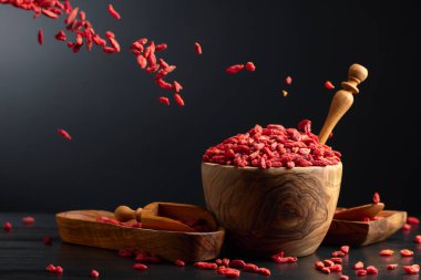 Siyah arka planda ahşap kasede kurutulmuş kurt üzümü. Çilekler hareket halinde.