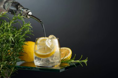 Buzlu, limonlu ve biberiyeli cin tonik. Cin şişeden buz ve limon dilimleriyle bardağa dökülür. Boşluğu kopyala.