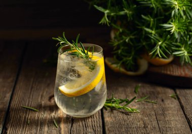 Eski ahşap bir masada buzlu, limonlu ve biberiyeli cin tonik. Boşluğu kopyala.