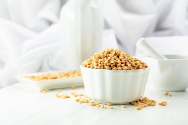 Beyaz ahşap bir masada soyulmuş çam fıstığı. Beyaz arka planda beyaz tabakta çam fıstığı.