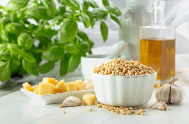 Pesto sosu yapmak için gerekli malzemeler. Fesleğen, çam fıstığı, sarımsak, parmesan ve beyaz ahşap bir masada zeytin yağı. Geleneksel İtalyan pesto tarifi.