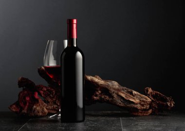 Siyah taş bir masanın üzerinde şişe ve bir bardak kırmızı şarap. Arka planda eski yıpranmış bir pürüz var. Kopyalama alanı ile ön görünüm.