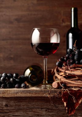 Eski ahşap bir masada üzümlü bir bardak ve bir şişe kırmızı şarap..