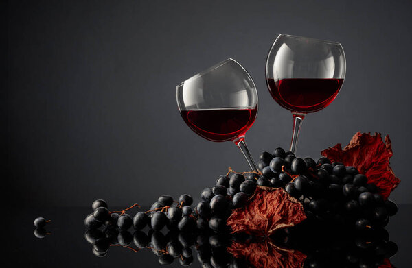 Glasses of red wine and blue grapes on a black background. Copy space.