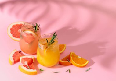 Greyfurt, portakal, biberiye ve buzlu yaz kokteylleri. İçkiler pembe arka planda, palmiye yaprağı gölgesinde. Yaz, tropikal, taze kokteyl konsepti.