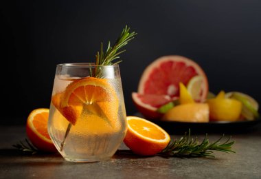 Buzlu, biberiyeli ve portakallı kokteyl cin toniği. Arka planda kokteyl yapmak için çeşitli turunçgil meyveleri var..