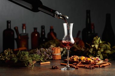 Esmer bitkisel likör ya da merhem eski bir şişeden bardağa dökülür. Kurutulmuş otlar, çiçekler, baharatlar ve eski mutfak aletleri. Bitkisel ilaç kavramı.