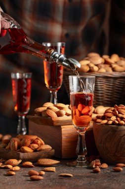 İtalyan likörü Amaretto. Eski bir masada badem fıstıklı. Likör şişeden bardağa dökülür..