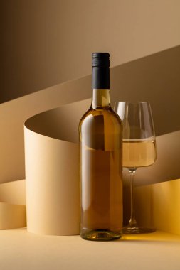 Bottle and glass of white wine on a beige background. Copy space.