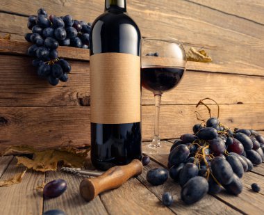 Eski ahşap bir masada bir şişe kırmızı şarap ve mavi üzüm. Eski boş bir şişede. Bir etikete odaklan.