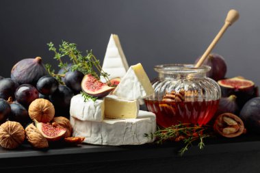 İncirli, üzümlü, cevizli, ballı ve kekikli Camembert peyniri. Siyah arka planda meyveli yumuşak peynir..