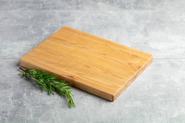 Taş bir masanın üzerinde kesme tahtası ve biberiye. Mutfak geçmişi. Boş tahta kesme tahtası, ürün görüntüleme alanı.