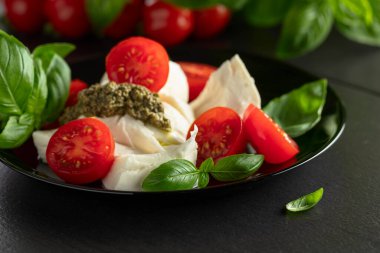 Fesleğenli Mozzarella, vişneli domates ve siyah tabakta pesto sosu. Geleneksel İtalyan mutfağı.