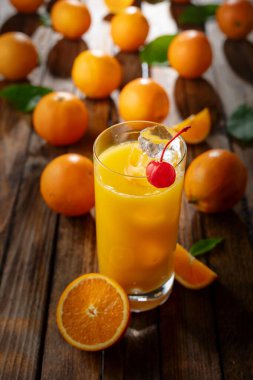 Kırmızı kirazla süslenmiş buzlu bir bardak portakal suyu. İçki ve taze meyveler eski ahşap bir masada.