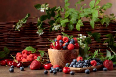 Bahçedeki eski ahşap bir masada çilek, yabanmersini, ahududu ve tatlı kiraz karışımının yakın plan renkli meyveleri. Yapraklı çeşitli meyveler.