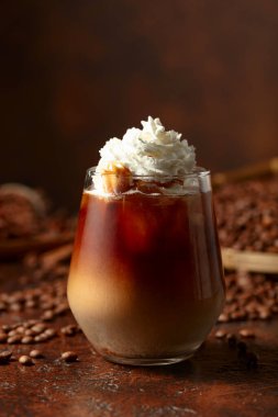 Krem şanti ve karamel soslu buzlu karamel latte. Kahverengi bir masada serinletici ve tatlı bir kahve..