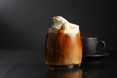 Krem şantili buzlu kahve ve karamel sosu ve siyah ahşap bir masada bir fincan sade kahve. Boşluğu kopyala.