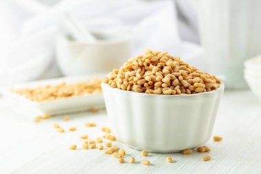 Beyaz ahşap bir masada soyulmuş çam fıstığı. Beyaz arka planda beyaz tabakta çam fıstığı.