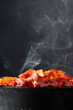 Siyah arka planda eski siyah bir tavada buharda pişmiş domuz pastırması. Boşluğu kopyala.