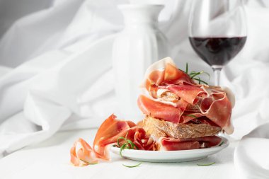 Ciabatta, prosciutto, biberiye ve beyaz ahşap bir masada bir bardak kırmızı şarap. Geleneksel İtalyan atıştırması.