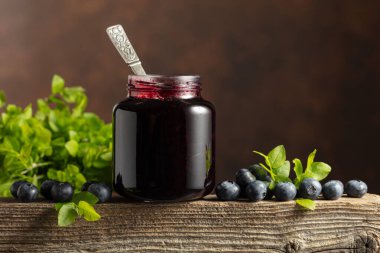 Bir kavanoz yabanmersini reçeli, taze böğürtlen ve eski ahşap bir masada yapraklar..