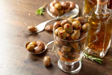 Baharatlı zeytin ve bir şişe zeytinyağı. Korunmuş zeytinler, zeytinyağı şişeleri ve ahşap bir masada biberiye dalları..