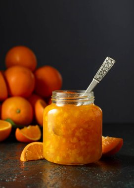 Cam kavanozda portakal reçeli ve koyu mavi bir masada taze meyve..