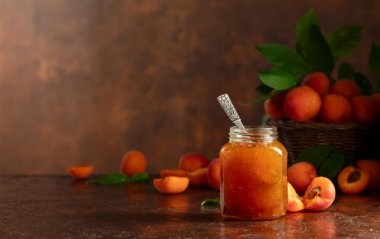 Cam kavanozda kayısı reçeli ve kahverengi bir masada taze meyve. Boşluğu kopyala.