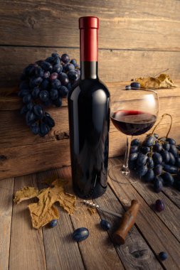 Eski ahşap bir masada mavi üzümlü bir şişe ve bir bardak kırmızı şarap..