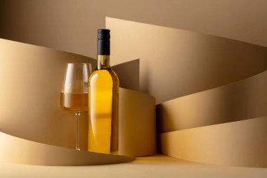 Bottle and glass of white wine on a beige background. Copy space.