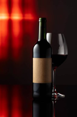 Siyah yansıtıcı arka planda cam ve bir şişe kırmızı şarap. Eski etiketli bir şişe kırmızı şarap. Metnin için alanı olan ön görünüm.