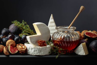 İncirli, üzümlü, cevizli, ballı ve kekikli Camembert peyniri. Siyah arka planda meyveli yumuşak peynir..