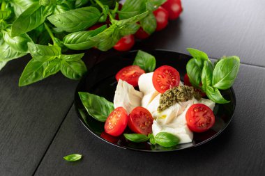 Fesleğenli Mozzarella, vişneli domates ve siyah tabakta pesto sosu. Geleneksel İtalyan mutfağı.