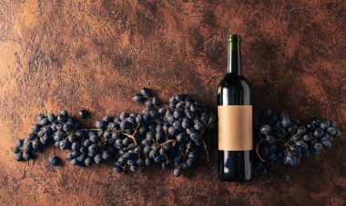 Kahverengi bir arka planda mavi üzüm ve bir şişe kırmızı şarap. Eski boş bir şişede. Boşluğu kopyala.