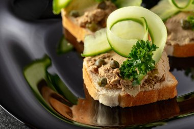Pate, taze salatalık, kapari ve maydanozlu sandviç. Siyah tabakta ezmeli tost..