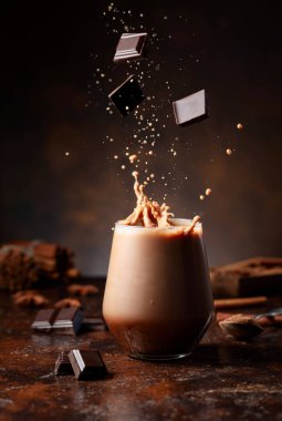 Koyu çikolata parçaları bir bardak kakao içeceğinin içine düşer ve güzel bir su sıçratır..