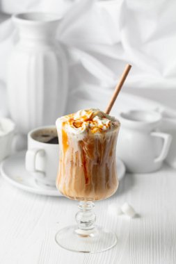 Krem şantili ve karamel soslu buzlu karamel latte, beyaz bir masada ferahlatıcı ve tatlı bir kahve..