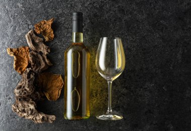 Siyah taşlı arka planda bir şişe beyaz şarap. Beyaz şarap, eski pürüzler ve kurumuş asma yaprakları. Üst Manzara. Boşluğu kopyala.