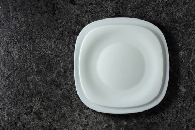 Siyah taş bir masanın üzerine boş beyaz tabaklar. Üst görünüm, alanı kopyala.