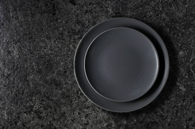 Siyah taş bir masanın üzerine boş siyah tabaklar. Üst görünüm, alanı kopyala.