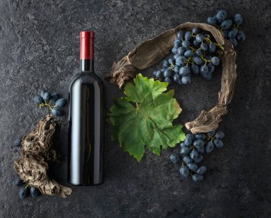 Bir şişe kırmızı şarap, mavi üzüm ve siyah taşlı arka planda eski asma parçaları. Üst Manzara. Boşluğu kopyala.