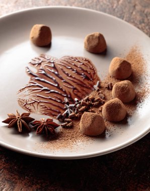 Bej bir tabakta çikolata soslu çikolatalı trüf mantarı. Şekerler kakao tozu, çikolata parçacıkları ve anason ile süslenir..