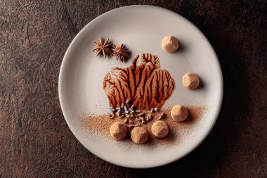 Bej bir tabakta çikolata soslu çikolatalı trüf mantarı. Tatlılar kakao tozu, çikolata parçacıkları ve anason ile süslenir. Yukarıdan görüntüle.