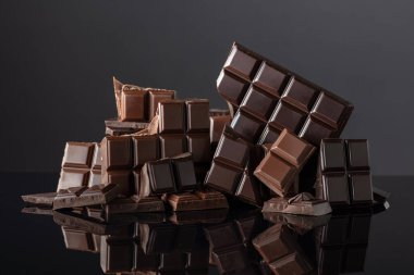 Siyah yansıtıcı arka planda kırık acı ve sütlü çikolatalar. Boşluğu kopyala.