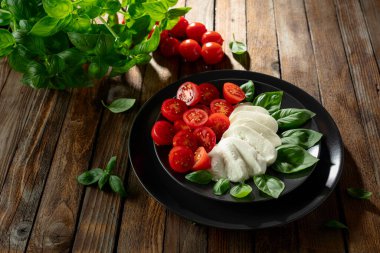 Eski ahşap bir masada fesleğen ve kiraz domatesli Mozzarella. Geleneksel İtalyan mutfağı.
